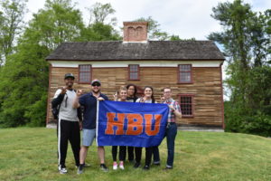 students stand outside of an old historical building in Boston holding an HBU flag